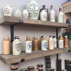 K&ouml;nnte beinhalten: Zwei Holzregale mit verschiedenen Glasflaschen und Gl&auml;sern. Die Flaschen sind aus klarem Glas mit wei&szlig;en Etiketten und einige haben braune Deckel. Die Gl&auml;ser sind wei&szlig; mit schwarzer Beschriftung. Die Regale sind aus braunem Holz mit schwarzen Metallhalterungen.