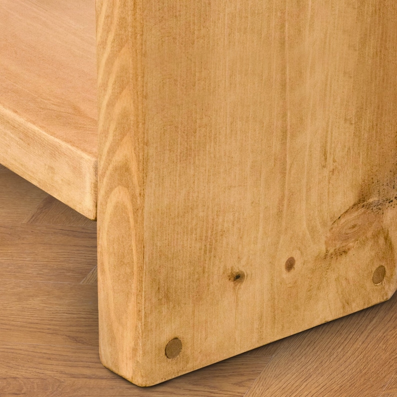 May include: Close-up of the bottom of a wooden shelf unit. The shelf is made of light brown wood with a natural finish. The shelf has a simple design with a rectangular shape and rounded edges. The shelf is supported by four metal brackets.