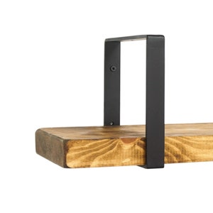Puede incluir: Una estantería de madera con soportes de metal negro. La estantería está hecha de madera natural con un acabado rústico. Los soportes son simples y de diseño moderno.