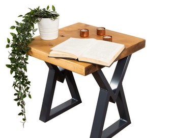 May include: A wooden side table with a natural wood finish and black metal legs. The table has a book and three small candles on top.