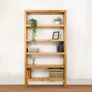 May include: A tall wooden bookshelf with five shelves. The shelves are filled with books, plants, and decorative items. The bookshelf is made of natural wood and has a rustic look.