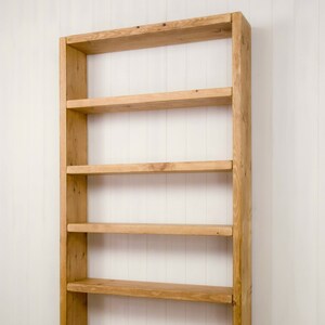 May include: A tall wooden bookshelf with five shelves. The shelves are made of natural wood and have a rustic look. The bookshelf is empty and ready to be filled with books or other items.