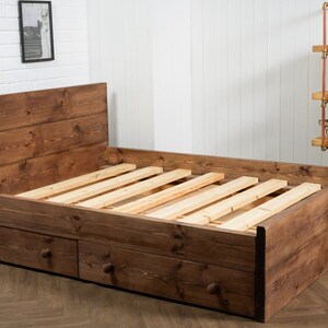 Puede incluir: Un marco de cama de madera r&uacute;stico con una cabecera y dos cajones. El marco de la cama est&aacute; hecho de madera marr&oacute;n oscura y tiene un acabado de madera natural. El marco de la cama tiene una base de listones y est&aacute; dise&ntilde;ado para un colch&oacute;n doble.