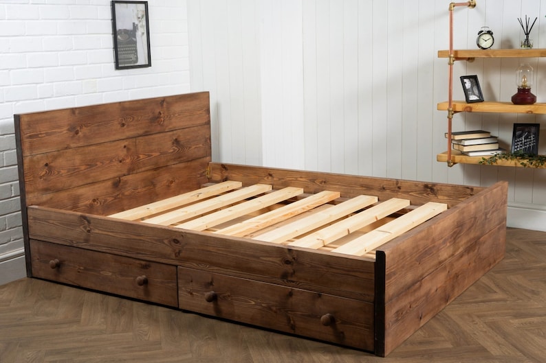 Puede incluir: Un marco de cama de madera r&uacute;stico con una cabecera y dos cajones. El marco de la cama est&aacute; hecho de madera marr&oacute;n oscura y tiene un acabado de madera natural. El marco de la cama tiene una base de listones y est&aacute; dise&ntilde;ado para un colch&oacute;n doble.