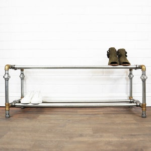 May include: A two-tiered shoe rack made of silver pipes and brass fittings. The rack has two shelves for storing shoes. There are two pairs of shoes on the rack, one pair of white trainers and one pair of green heeled sandals.