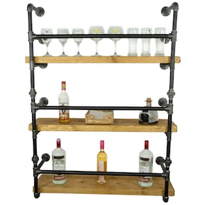 May include: A three-tiered wall-mounted shelf unit made of black metal pipes and wooden shelves. The shelves are filled with bottles of liquor and wine glasses.