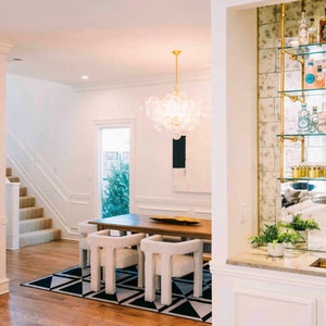 May include: A white dining room with a large glass chandelier, a wooden table with white chairs, and a mirrored bar with gold shelves and bottles.