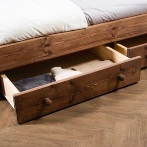 Puede incluir: Un marco de cama de madera con dos cajones extra&iacute;dos, revelando ropa doblada en el interior. Los cajones tienen pomos de madera y est&aacute;n hechos del mismo madera marr&oacute;n oscuro que el marco de la cama.