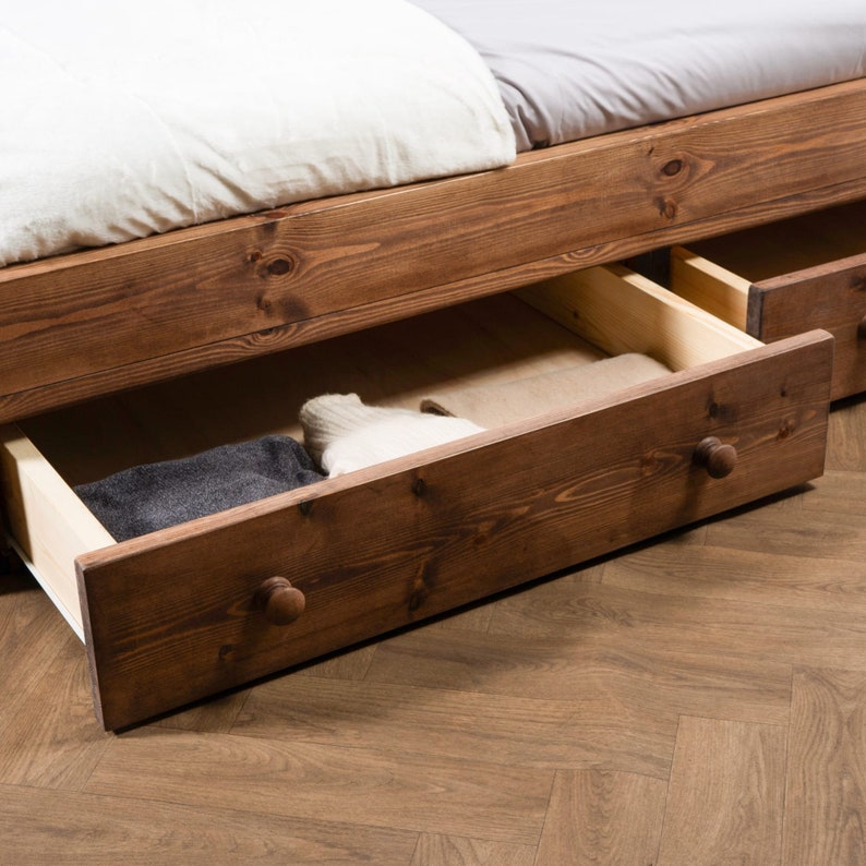Puede incluir: Un marco de cama de madera con dos cajones extra&iacute;dos, revelando ropa doblada en el interior. Los cajones tienen pomos de madera y est&aacute;n hechos del mismo madera marr&oacute;n oscuro que el marco de la cama.