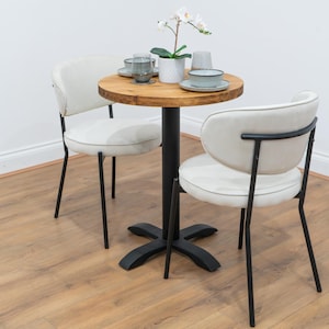 May include: A small dining set with a round wooden table and a black pedestal base, plus two chairs. The chairs have white cushioned seats and backs with black metal frames. The table is set with plates, glasses and a potted plant.