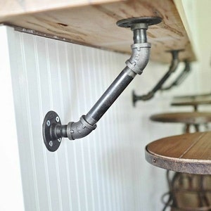 May include: A close-up of a black metal pipe shelf bracket attached to a white wall. The bracket is supporting a wooden countertop.