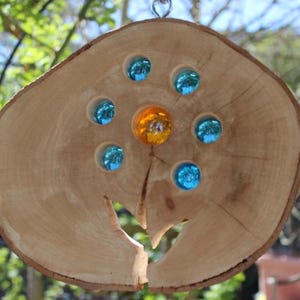 Op de afbeelding: Een houten cirkel met een uitsparing in de vorm van een hand. De cirkel is versierd met blauwe en gele glazen knikkers.
