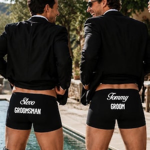 May include: Four black boxer briefs featuring white printed text on the back. The text reads Pete BEST MAN, Slevo GROOMSMAN, Tommy GROOM, and Liam GROOMSMAN. Each pair of underwear is worn by an individual wearing a black suit jacket and lowered trousers.