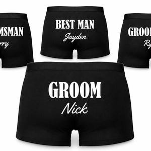 May include: Four pairs of black boxer briefs featuring white printed text. The top three pairs are labelled GROOMSMAN Harry, BEST MAN Jayden, and GROOMSMAN Ryan. The larger bottom pair is labelled GROOM with the name Nick printed underneath in white.