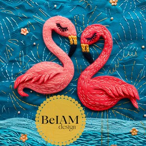Op de afbeelding: Twee geborduurde flamingo's in roze en rood, met zwarte snavels en gouden accenten, tegen een turquoise achtergrond met bloemen- en golfdetails. Het ontwerp bevat de tekst "BeIAM design" in een gele cirkel.