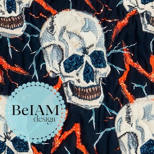 Puede incluir: Tela negra con calaveras blancas bordadas y rayos naranjas. Las calaveras tienen ojos de purpurina azul y un fondo blanco. La tela tiene un logotipo "BeIAM design" en el centro.