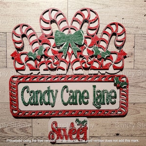May include: A wooden sign with a red and white candy cane design and the words "Candy Cane Lane" in green letters. Below the sign is a smaller wooden sign with the word "Sweet" in red letters.