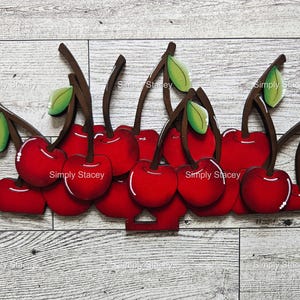 May include: A cluster of red cherries with green leaves, painted on wood, arranged in a row. The cherries are all the same size and shape, and they are all facing the same direction. The leaves are all the same size and shape, and they are all facing the same direction.
