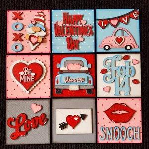 May include: Nine square wooden signs with Valentine's Day themes. The signs feature red, pink, blue, and white colors with glitter accents. The signs include phrases like "Happy Valentine's Day", "Be Mine", "Love", "XOXO", "Kisses 25¢", "Feb 14", and "Smooch".