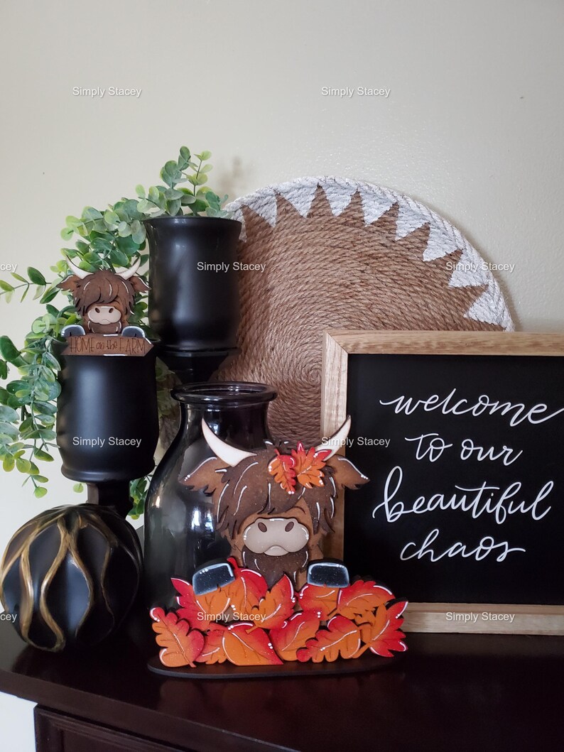 May include: A wooden Highland Cow figurine with fall leaves, a black chalkboard sign with the text "welcome to our beautiful chaos", and a black and gold decorative orb.