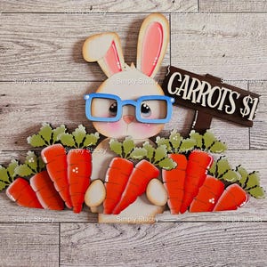 May include: A white bunny wearing blue glasses holds a sign that says "Carrots $1". The bunny is surrounded by carrots with green tops.