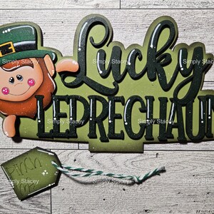 May include: A green, black, and white wooden sign with the words "Lucky Leprechaun" and a cartoon leprechaun with a green hat and beard. The sign has a small green tag attached to it that says "Pinch Me".