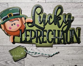 May include: A green, black, and white wooden sign with the words "Lucky Leprechaun" and a cartoon leprechaun with a green hat and beard. The sign has a small green tag attached to it that says "Pinch Me".