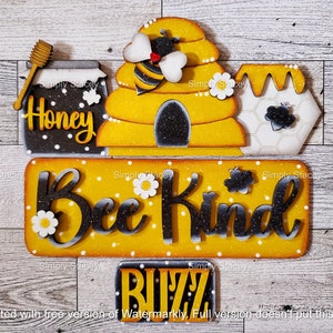 May include: A wooden sign with a bee theme. It features a yellow and black beehive, a jar of honey, and the words "Bee Kind" and "Buzz". The sign is decorated with daisies and a bee.