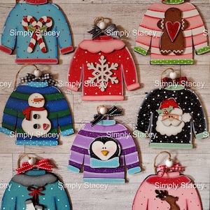May include: Eight hand-painted wooden ornaments shaped like sweaters with different holiday-themed designs. The ornaments are decorated with candy canes, snowmen, penguins, reindeer, gingerbread men, snowflakes, and Santa Claus. Each ornament has a white bead and a brown twine hanger. The ornaments are arranged in a circle on a wooden background. The text "Simply Stacey" appears on each ornament.