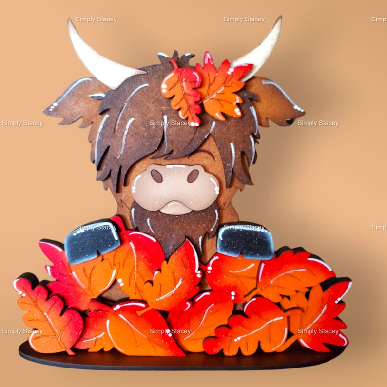 May include: A wooden Highland Cow figurine with brown fur and a black nose, surrounded by orange and red painted leaves. The figurine is standing on a black base.