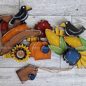 May include: A set of wooden cutouts for a fall-themed craft project. The set includes a scarecrow hat, two black birds, a pumpkin, corn, sunflowers, and a sign that says "Build a Scarecrow".
