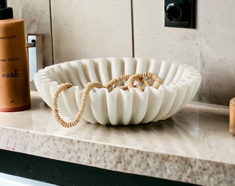 May include: A white marble bowl with a fluted design, filled with a pile of brown hair ties.