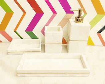May include: White marble bathroom accessories set with gold accents. The set includes a soap dispenser, toothbrush holder, soap dish, and a tray.