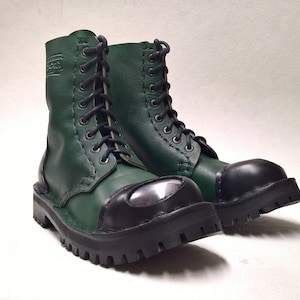May include: A pair of dark green leather boots with black toe caps and silver metal accents. The boots have laces and are made of a durable material.