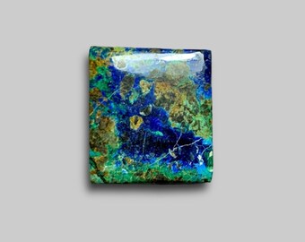 May include: Square-shaped azurite gemstone with a polished surface. The stone features a mix of deep blue, green, and brown hues, with a glossy finish. The gemstone is set against a neutral background.