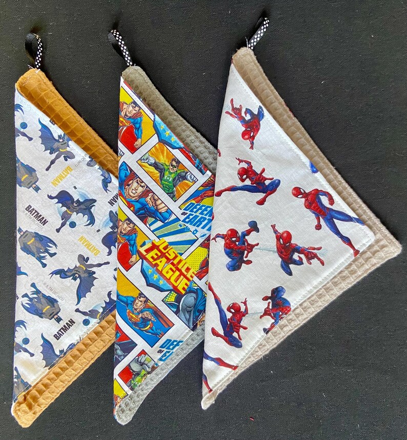 Pu&ograve; includere: Tre strofinacci da cucina triangolari con disegni di supereroi. Uno presenta Batman, un altro la Justice League e il terzo Spiderman. Ogni strofinaccio ha un bordo a nido d'ape e un anello per appenderlo.