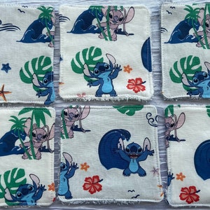 Può includere: Sei sottobicchieri quadrati in tessuto con un motivo ripetuto con il personaggio Stitch di Lilo & Stitch. Il design include Stitch, onde, palme e fiori tropicali in blu, verde e rosso su sfondo crema.