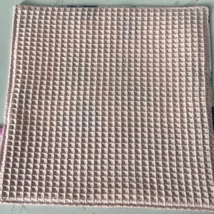 May include: A pale pink waffle weave kitchen towel. The towel is made of a soft, absorbent material and is perfect for drying dishes, hands, and surfaces.