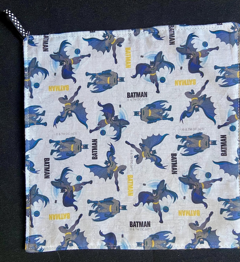 Pu&ograve; includere: Tessuto quadrato e chiaro con un motivo ripetuto di personaggi di Batman in varie pose. La parola "BATMAN" &egrave; stampata in giallo. Il tessuto ha un passante a pois bianchi e neri.