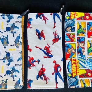 Pu&ograve; includere: Tre custodie in tessuto con disegni di supereroi. Una presenta loghi e testo di Batman, un'altra Spider-Man e la terza pannelli di fumetti della Justice League. Ogni custodia ha un nastro a pois bianco e nero.