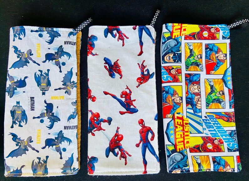 Pu&ograve; includere: Tre custodie in tessuto con disegni di supereroi. Una presenta loghi e testo di Batman, un'altra Spider-Man e la terza pannelli di fumetti della Justice League. Ogni custodia ha un nastro a pois bianco e nero.