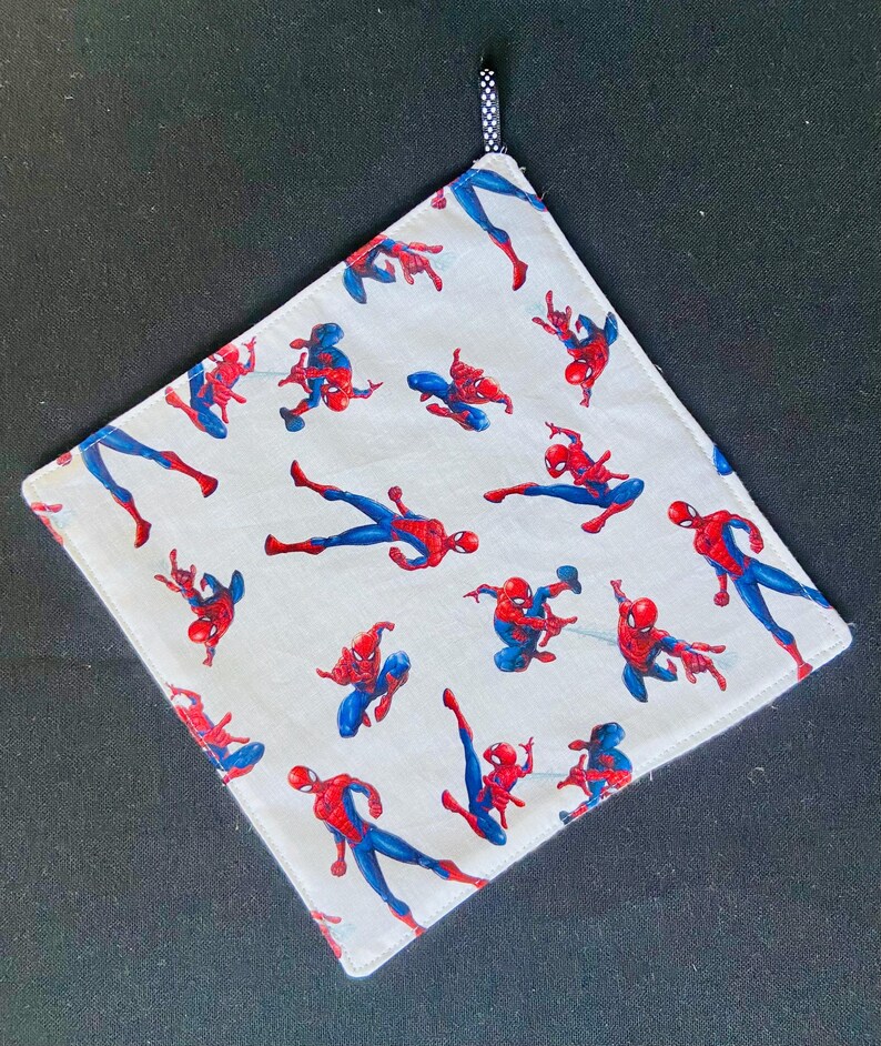 Pu&ograve; includere: Tessuto quadrato bianco con un motivo ripetuto di figure di Spider-Man rosse e blu. Un anello a pois bianchi e neri &egrave; attaccato a un angolo. I bordi sono rifiniti con una cucitura rossa.