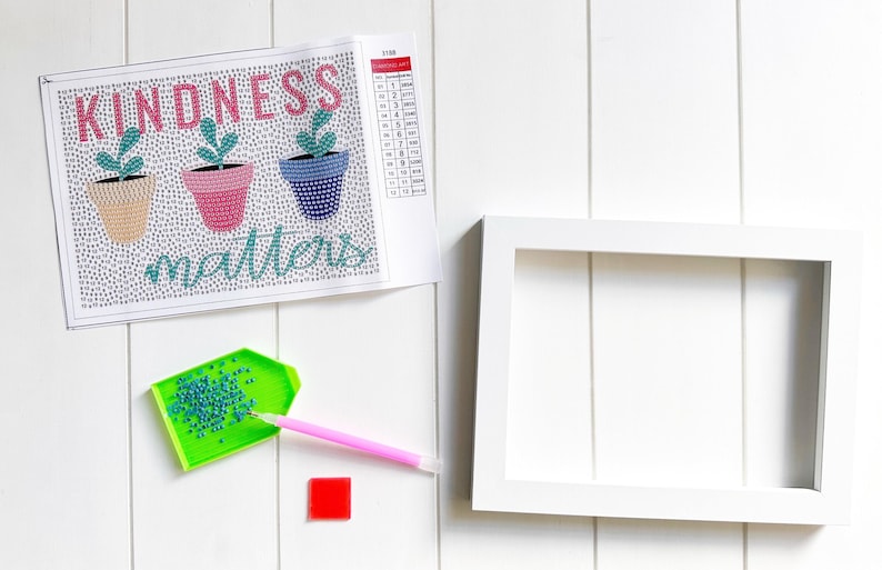 May include: A diamond painting kit with a white background and a colorful design of three potted plants with the text "Kindness matters". The kit includes a tray of diamonds, a pen, and a white frame.