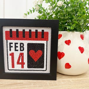 May include: A black framed picture with a red, white, and black calendar design. The calendar says "FEB 14" with a red heart in the center.