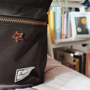 A black backpack with a gold zipper and a small gold star pin with a smiley face.