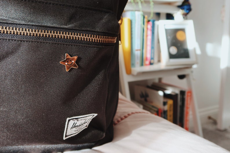 A black backpack with a gold zipper and a small gold star pin with a smiley face.
