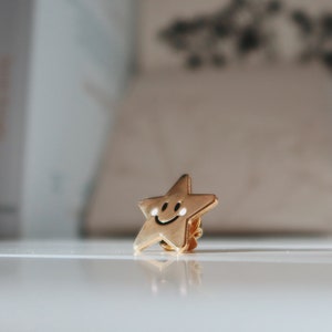 A gold-coloured star-shaped pin with a smiling face.