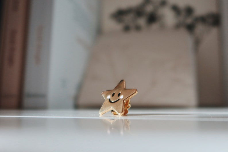 A gold-coloured star-shaped pin with a smiling face.