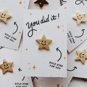 A pile of gold star pins with a smiley face on each star. The pins are attached to cards that say "You did it!" and "Gold Star for You".