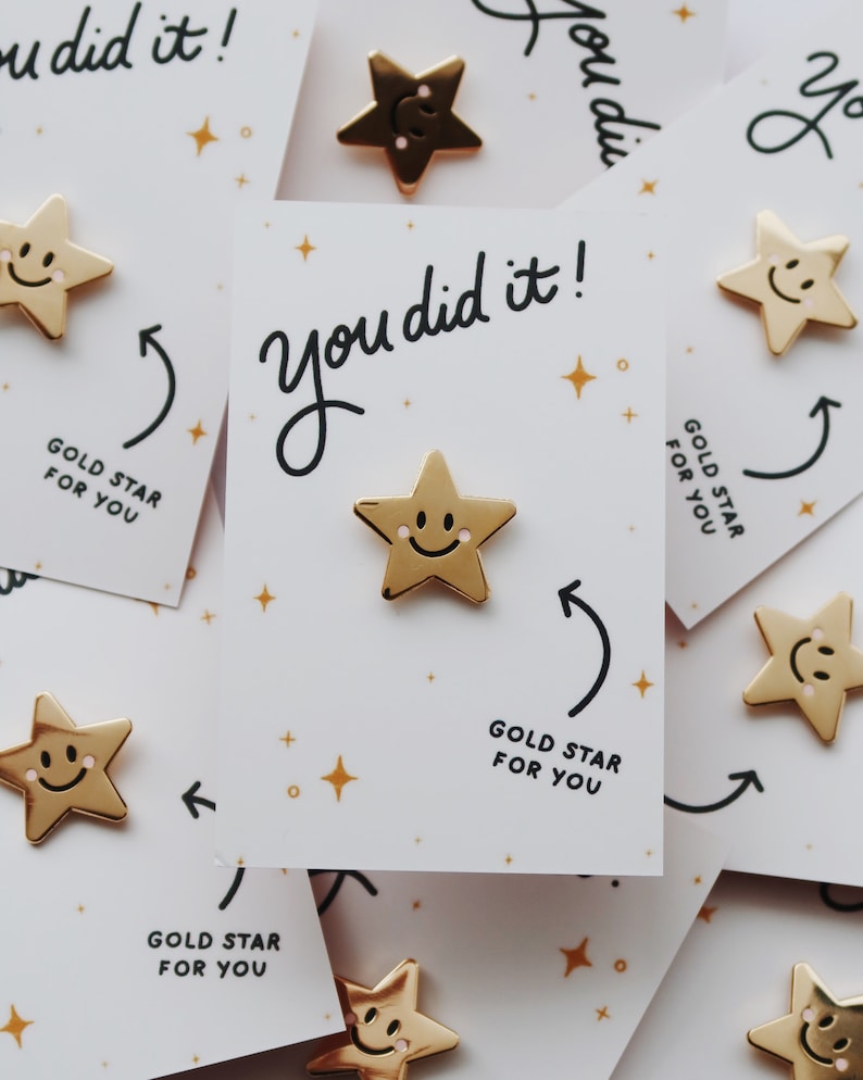A pile of gold star pins with a smiley face on each star. The pins are attached to cards that say "You did it!" and "Gold Star for You".